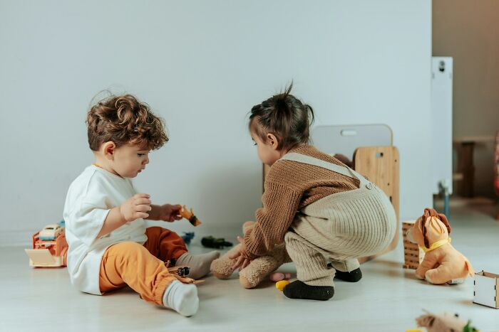Two toddlers playing on the floor with toys, illustrating signs of being stuck in their high school era later in life.
