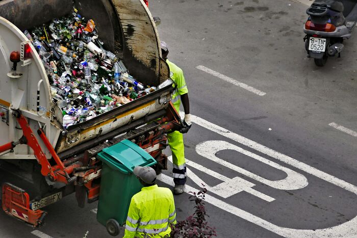 Two sanitation workers in bright yellow uniforms collecting recyclables in a garbage truck on city street cleaning industry truths