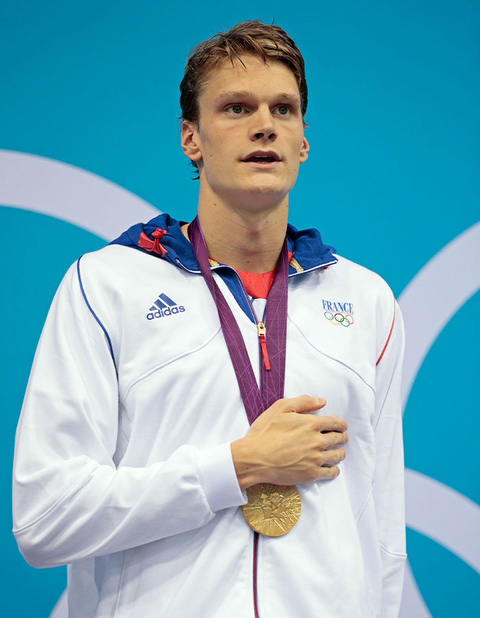 Young Olympic gold medalist wearing white France jacket with gold medal at his neck during award ceremony