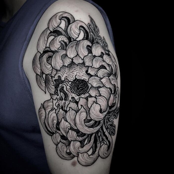 Intricate black and gray tattoo of a skull entwined with swirling floral patterns on a person’s upper arm.
