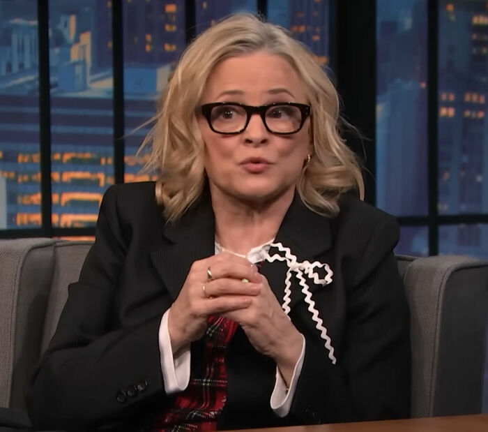 Amy Sedaris wearing black glasses and a blazer, speaking during a televised New Year's Eve broadcast on CNN.