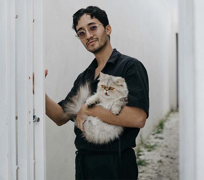 Man holding a fluffy cat outside a white building, illustrating a cat disappearing for days and being adopted by a neighbor.