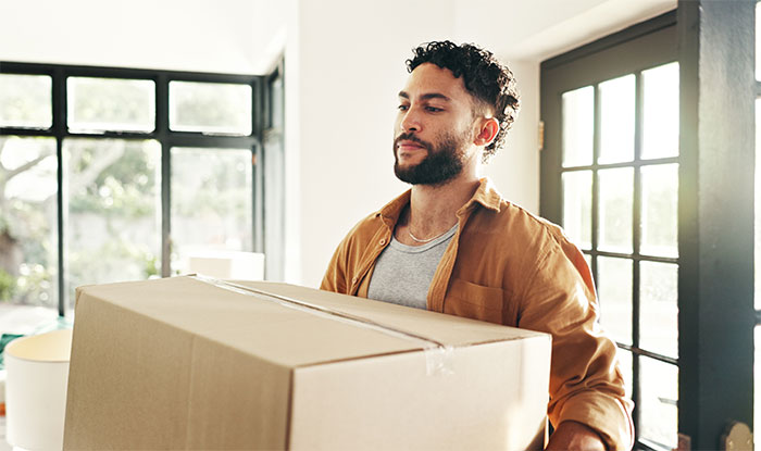 Man moving large box into home, representing man accidentally moves in next door to former friend conflict story. Man moving large box into home, representing man accidentally moves in next door to former friend conflict story.