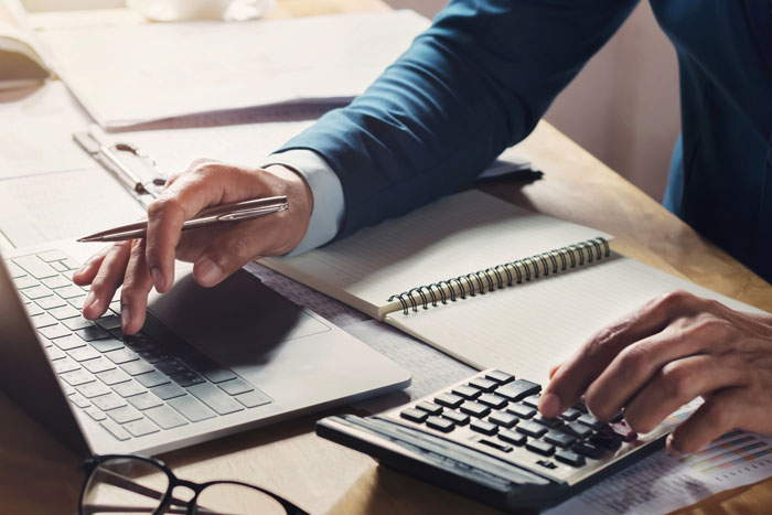 Person using a calculator and laptop at a desk with a notebook, managing finances related to emptying father's estate. Person using a calculator and laptop at a desk with a notebook, managing finances related to emptying father's estate.