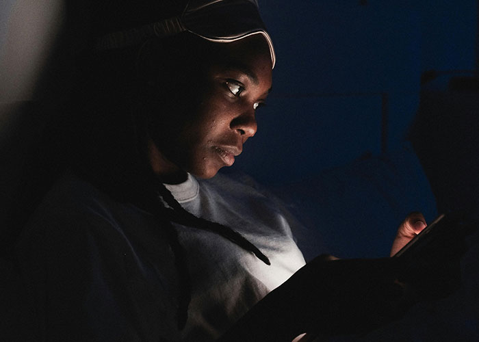 Woman in dim light looking at phone, reflecting on discovering her boyfriend is an internet troll and victim of trolling.