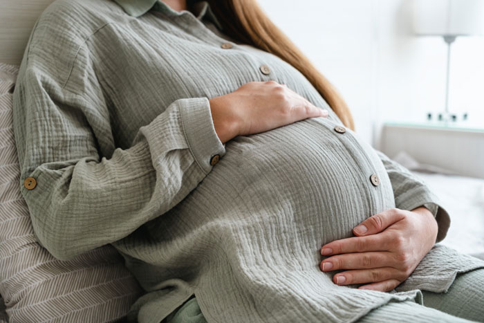 Pregnant woman resting on bed with hands on belly, facing a dilemma about fianc&eacute;&rsquo;s mom in delivery room.
