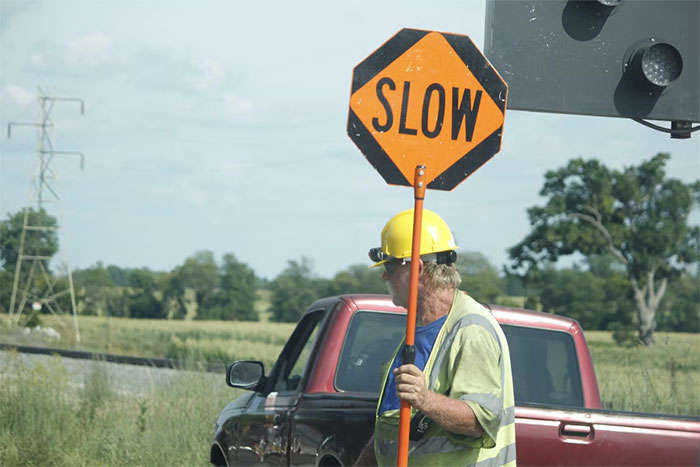 Man in safety vest holding slow sign near a pickup truck, illustrating anxiety meltdown risk while driving safety.