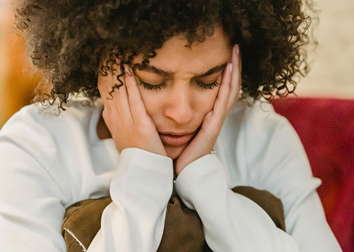 Woman looking distressed, holding her face with hands, reflecting feelings after skipping sister's birthday party event Woman looking distressed, holding her face with hands, reflecting feelings after skipping sister's birthday party event