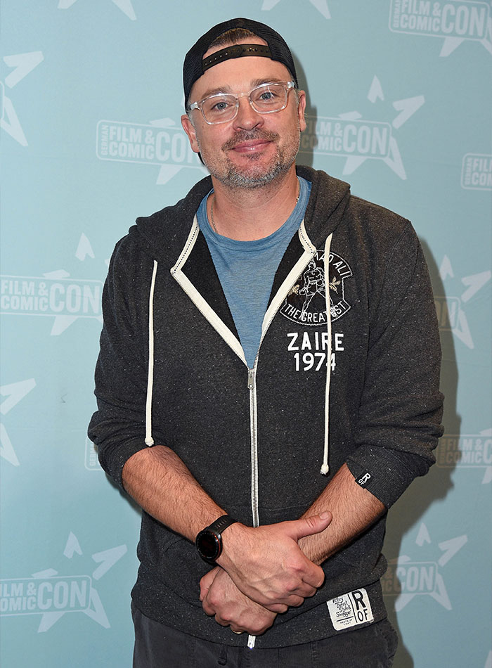 Man at a fan convention wearing glasses, a black cap, and a dark hoodie, a 2000s teen heartthrob now aged 48. Man at a fan convention wearing glasses, a black cap, and a dark hoodie, a 2000s teen heartthrob now aged 48.