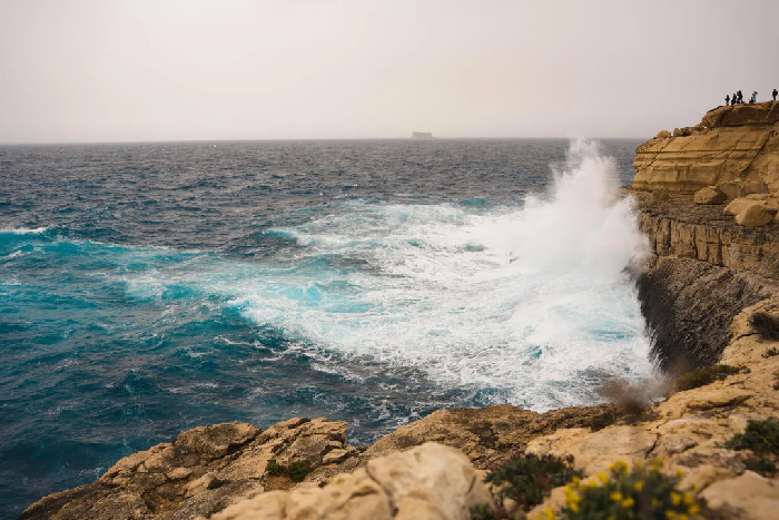 Rough sea crashing on rocky cliffs with people watching, evoking Most Stressful Countries