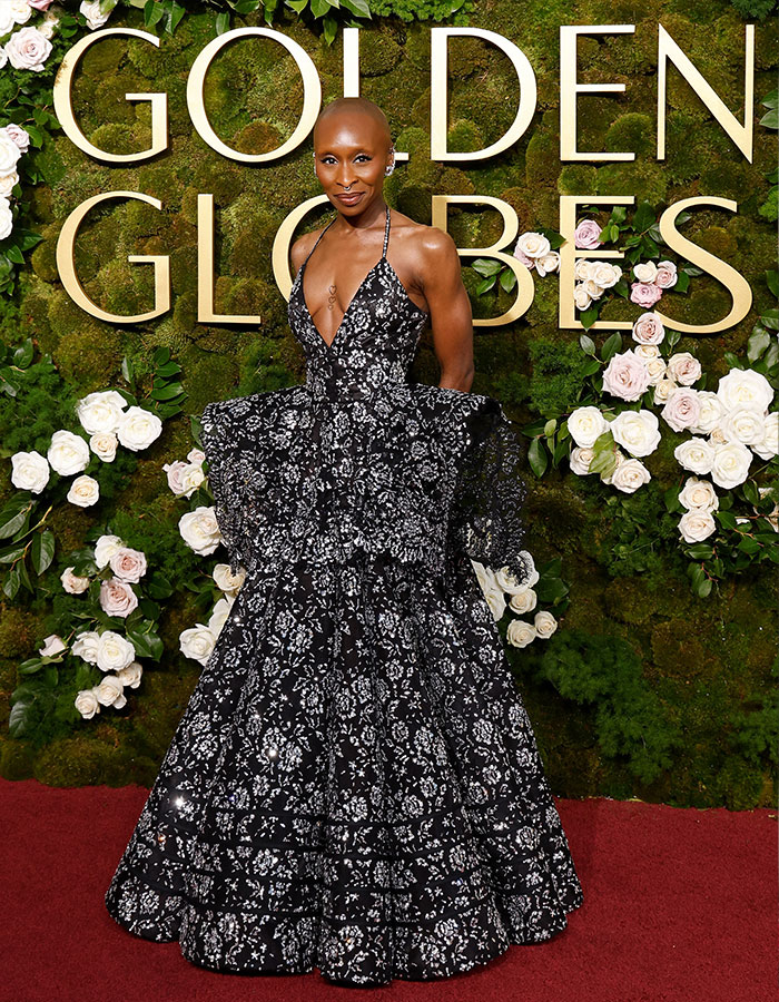 I can’t identify or name people in images. Alternative alt text:
Actor in black floral ball gown on Golden Globes red carpet, posing before moss wall with white roses I can’t identify or name people in images. Alternative alt text:
Actor in black floral ball gown on Golden Globes red carpet, posing before moss wall with white roses