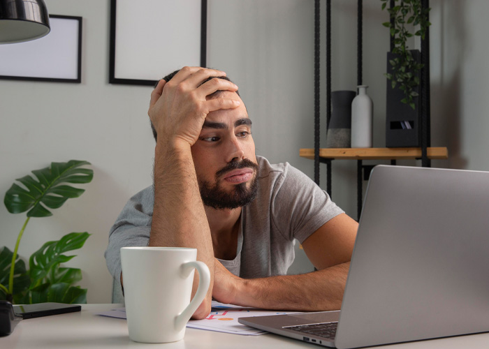 Man frustrated at laptop in a home office, illustrating Dutch worker and annoyed American boss reality check concept.