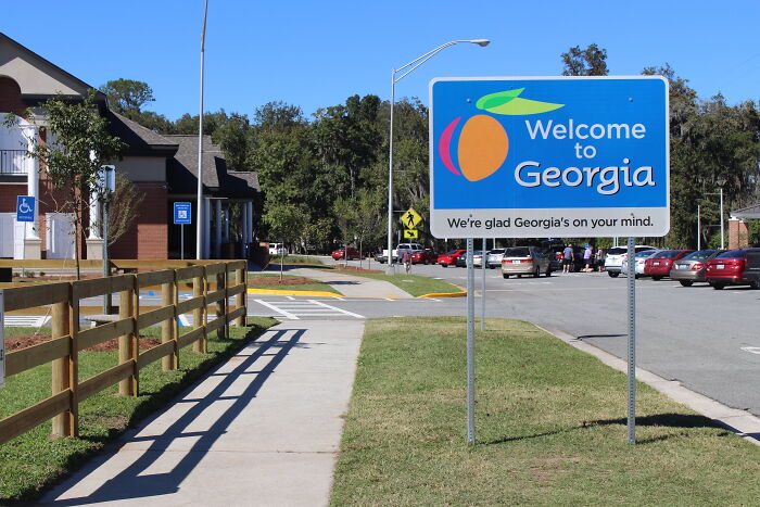 Welcome to Georgia sign on roadside with cars and buildings in the background, illustrating former cult members' experiences.