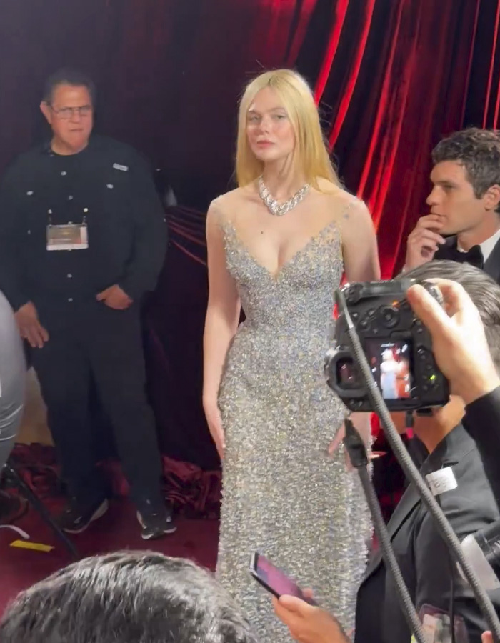 Elle Fanning in a sparkling gown at an event, with photographers capturing her electric head look on the red carpet.