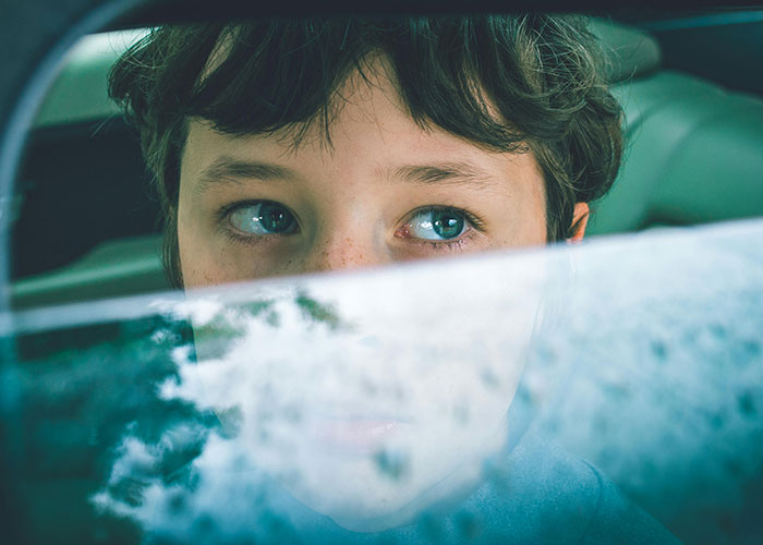 Young boy with curious eyes looking through a car window, illustrating wacky stories and unusual experiences shared by people.