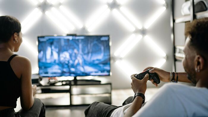 Two people playing video games on a console, focused on the screen in a modern living room setting.