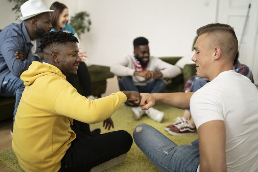 Group of friends sitting and fist bumping indoors, enjoying paranoia questions and social interaction games together.