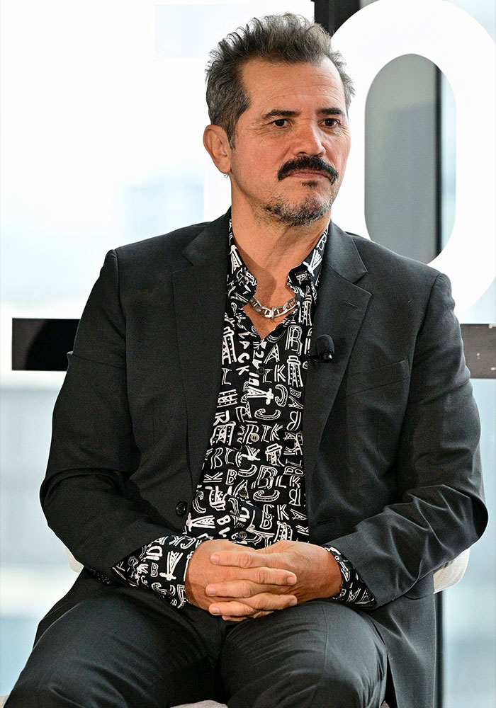 Star actor wearing a black suit and patterned shirt, seated with hands clasped, under fire after telling fans to choose between him and ICE.