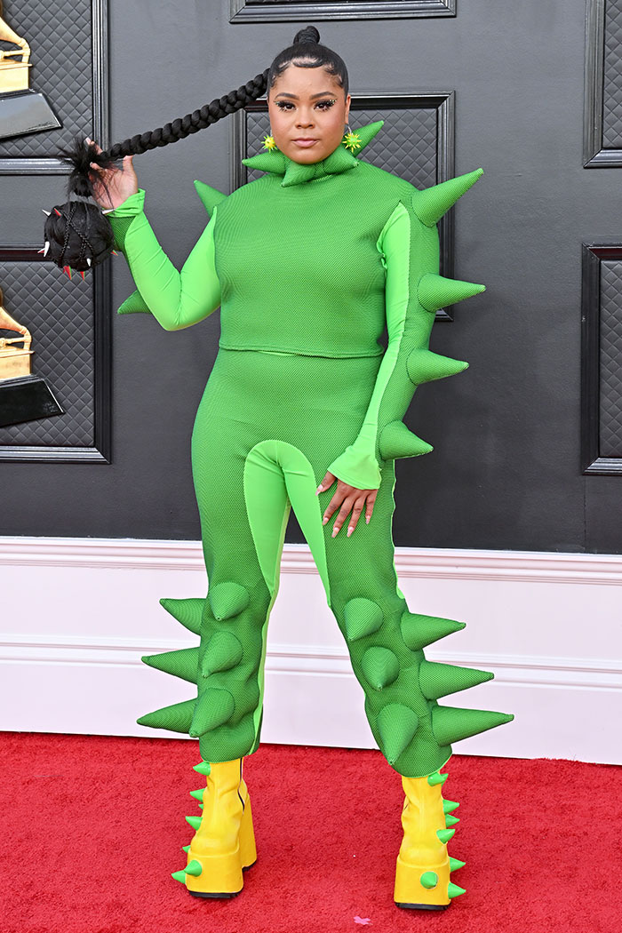 Woman in spiked green outfit with matching yellow spiked boots on the Grammys red carpet showcasing wild Grammys looks.