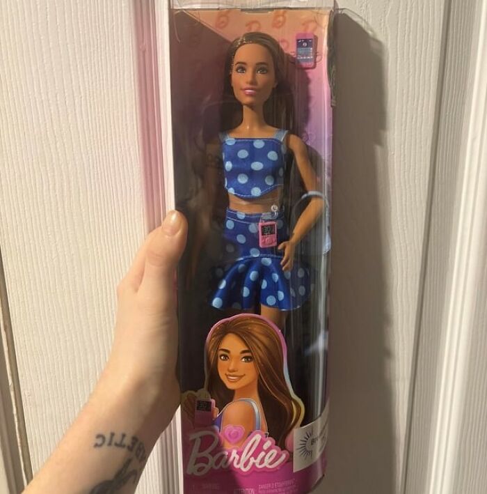 Barbie doll in blue polka dot outfit held in hand, representing uplifting stories of progress and hope in America.