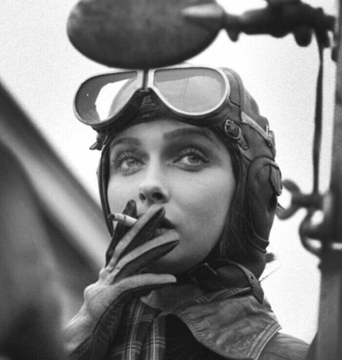 Black and white photograph of a woman pilot smoking a cigarette, capturing a poignant moment in the history of humanity.