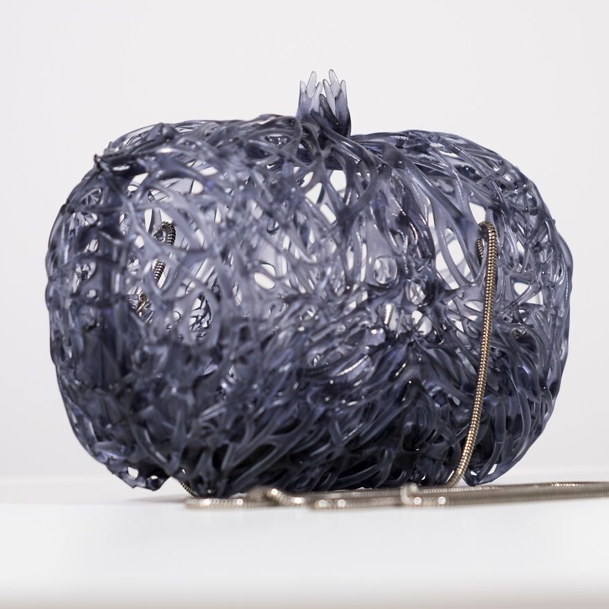 Intricate dark biomimicry-inspired structure resembling natural patterns with a thin metallic chain on a light surface.