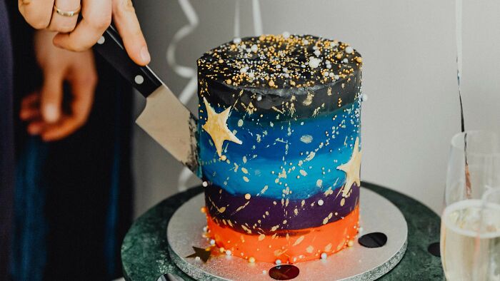 Person cutting a colorful galaxy-themed cake decorated with stars, inviting opinions on whether they did the right thing.