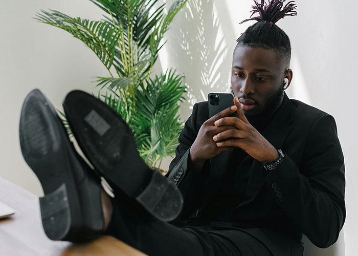 Man in a black suit with earbuds, looking at smartphone, illustrating neurodivergent behaviors and self-awareness.