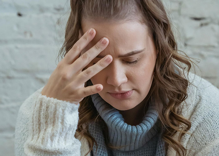 Woman in a gray sweater with hand on forehead looking stressed, reflecting on kids with no filter family lore stories.