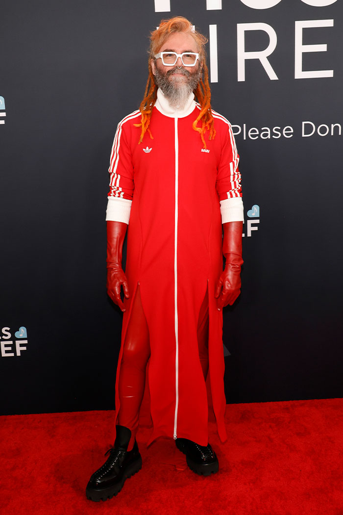 Man with orange dreadlocks and beard wearing a red Adidas outfit and gloves on the red carpet at Grammys event.