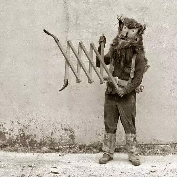 Person in an old black and white photo wearing a creepy animal mask and holding a strange expandable wooden tool.
