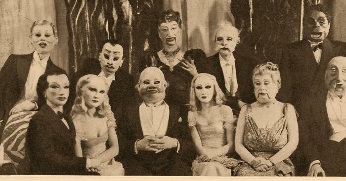 Group of people in old black and white photo wearing odd and creepy masks, creating a haunting vintage atmosphere.
