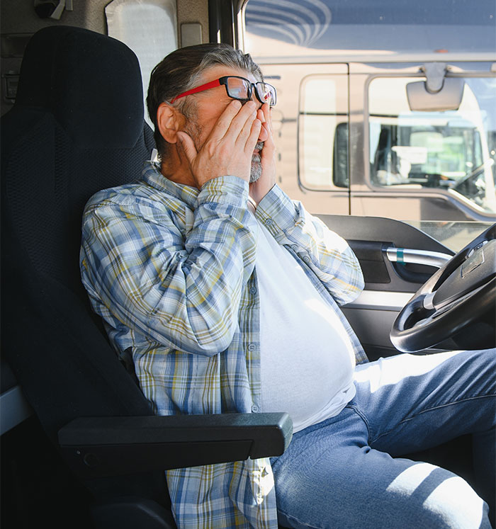 Man in a plaid shirt sitting in a truck cabin, covering his face in shock, illustrating workplace bully revenge theatrics.