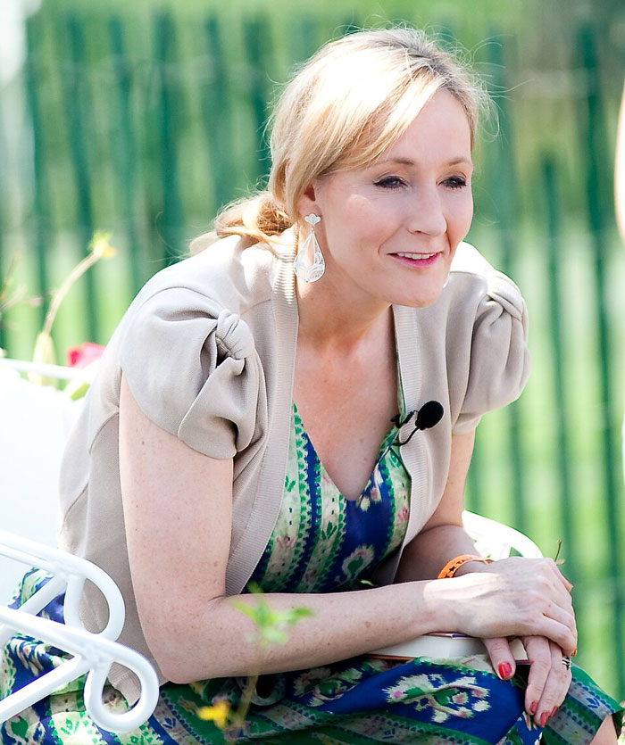 Blonde woman sitting outdoors in patterned dress and beige shrug, appearing thoughtful about celebrities whose careers crashed and never recovered.