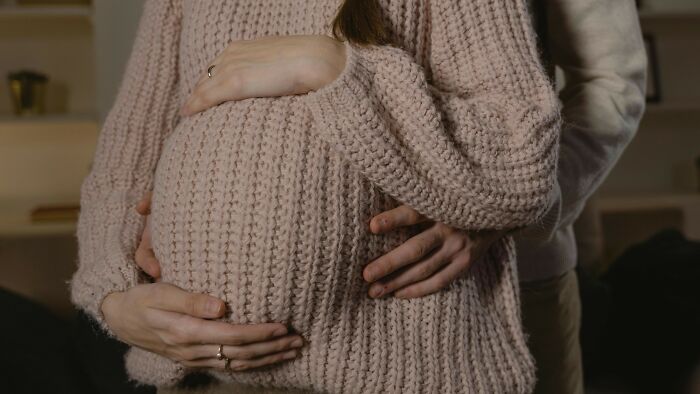 Couple embracing while woman in a pink knitted sweater shows pregnant belly, illustrating people who did the right thing.