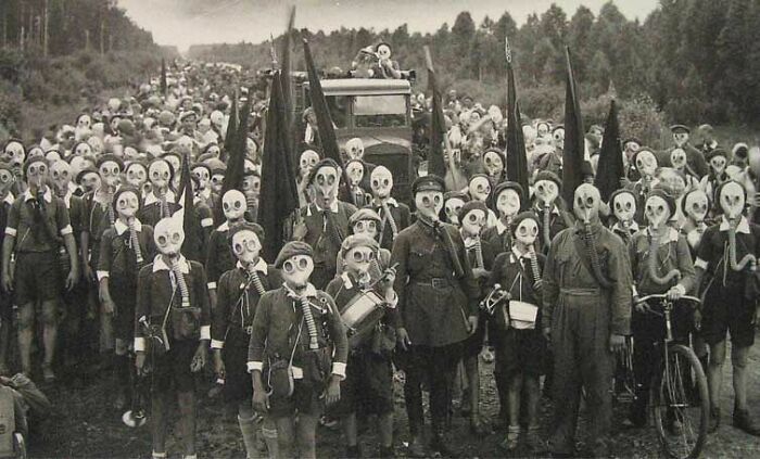 Group of people wearing vintage gas masks in an old black and white creepy photo with an odd atmosphere.