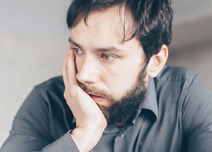 Bearded man in a gray shirt looking pensive, reflecting on life after discovering he isn’t the biological parent.
