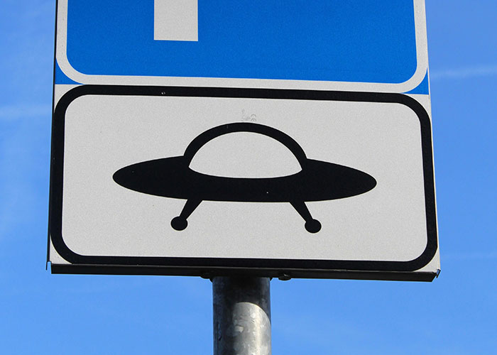 UFO road sign under clear blue sky representing wacky stories people share hoping someone will believe them.