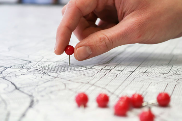 Hand placing a red pushpin on a detailed map, showcasing smart and borderline creepy precision and planning.