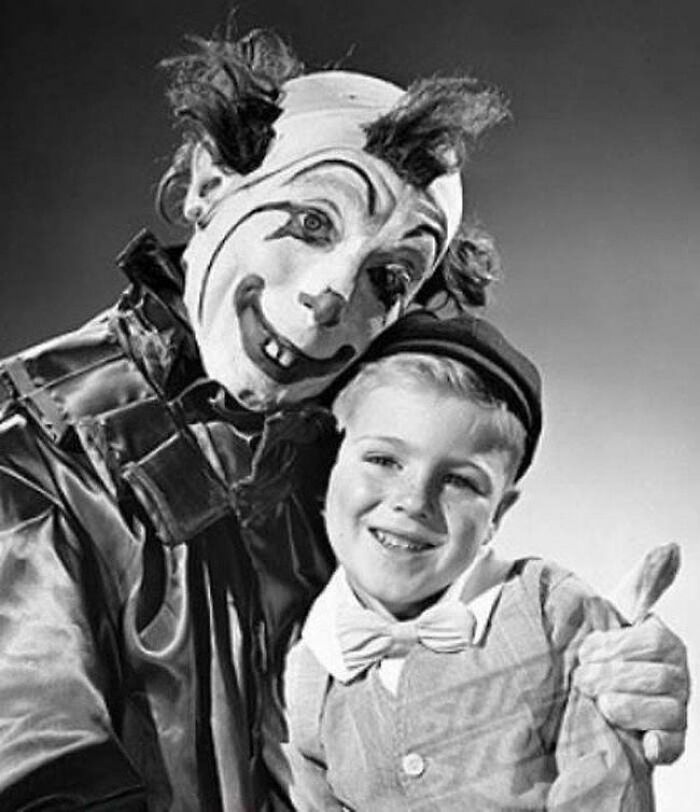 Black and white vintage photo of a creepy clown with exaggerated makeup posing with a smiling young boy.