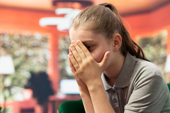 Young woman in a service industry setting covering her face, experiencing an awkward moment at work.