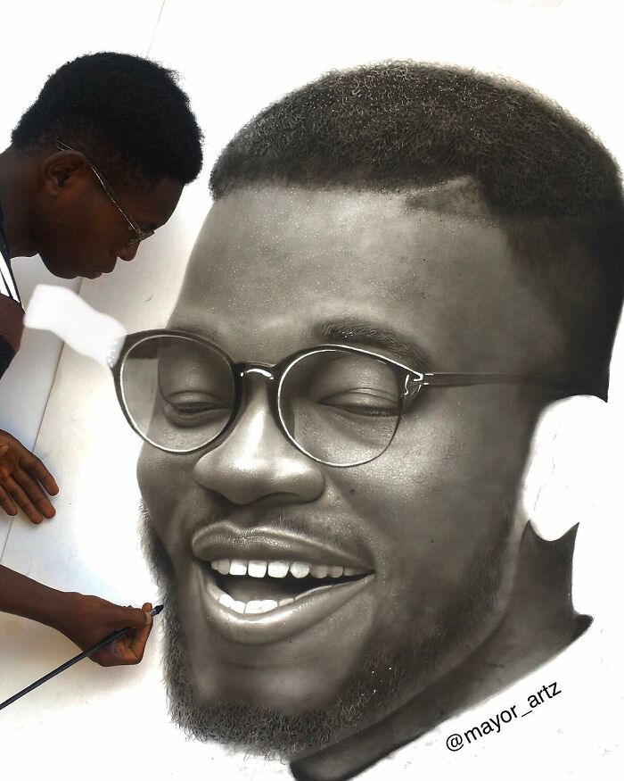 Artist creating a hyperrealistic portrait with detailed shading of a smiling man wearing round glasses.