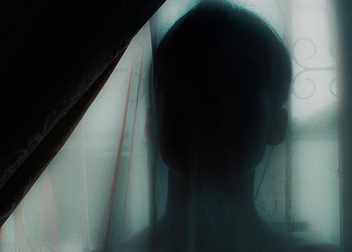 Silhouetted person behind sheer curtain in dim light, representing wacky stories shared by people hoping to be believed.