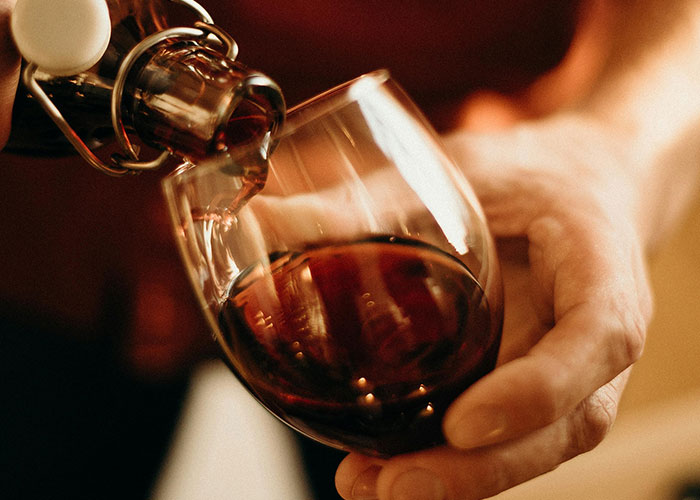 Pouring red wine into a glass held by a hand, illustrating casual moments in family lore discussions.