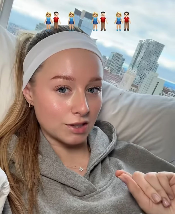 Young woman sharing story about having 7 parents, seated indoors with city skyline visible through window behind her. Young woman sharing story about having 7 parents, seated indoors with city skyline visible through window behind her.