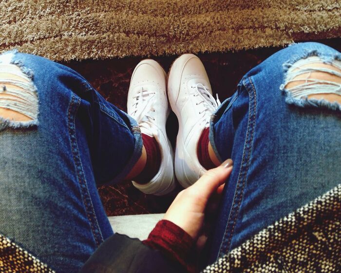 Person wearing ripped jeans and white sneakers sitting on a carpet, illustrating things normal in America but offensive elsewhere.