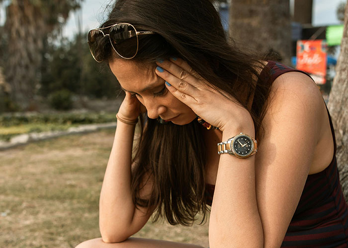 Woman sitting outdoors with hands on her head, illustrating habits neurodivergent people thought were normal.