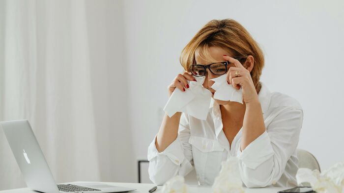 Woman in glasses wiping tears with tissue while sitting at desk with laptop, reflecting if she did the right thing.