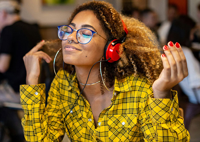 Young woman with curly hair and glasses wearing red headphones, enjoying music, representing neurodivergent habits awareness.