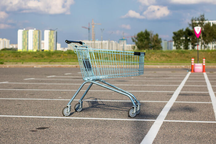 Empty shopping cart abandoned in a large parking lot, illustrating weird and satisfying situations not my problem anymore.